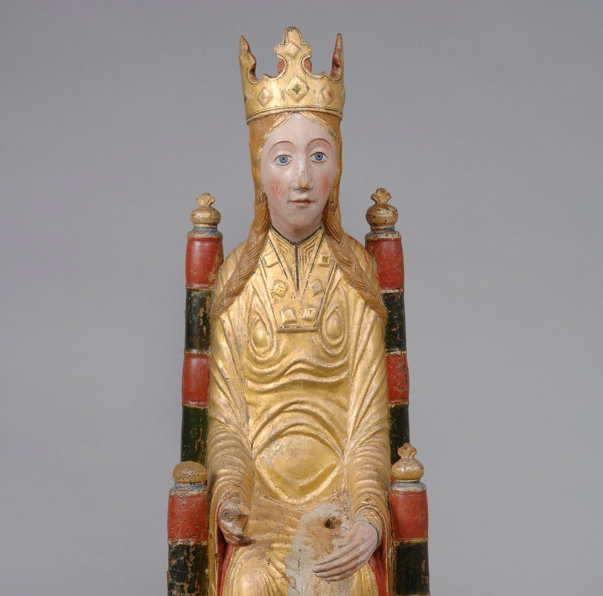 Foto av en träskulptur som föreställer en madonna. Skulpturen är målad i guld, rött och svart