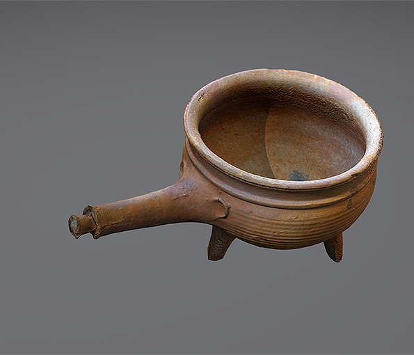 Rund keramikgryta på tre ben med ett handtag som sticker rakt ut från sidan, som en pinne.