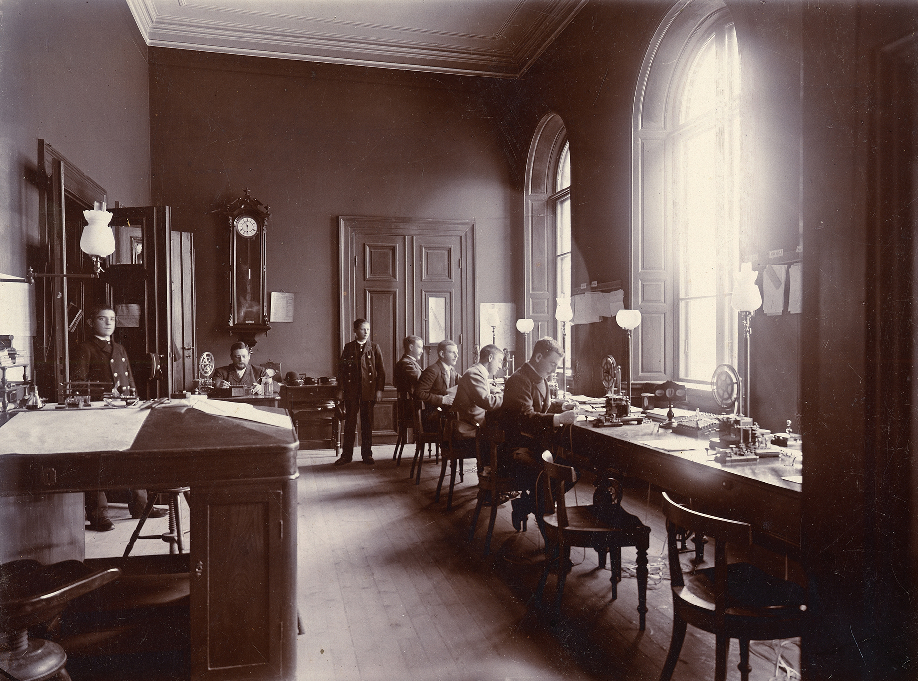 En sal med ett långt bord där det sitter män vid telegrafmaskiner.