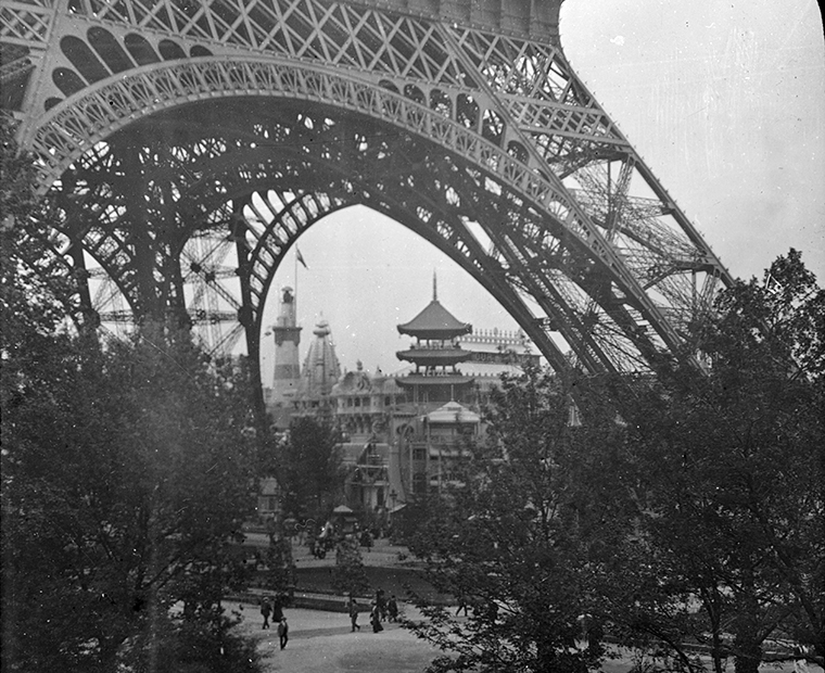 Genom nedre delen av Eiffeltornet ser man träd och byggnader.