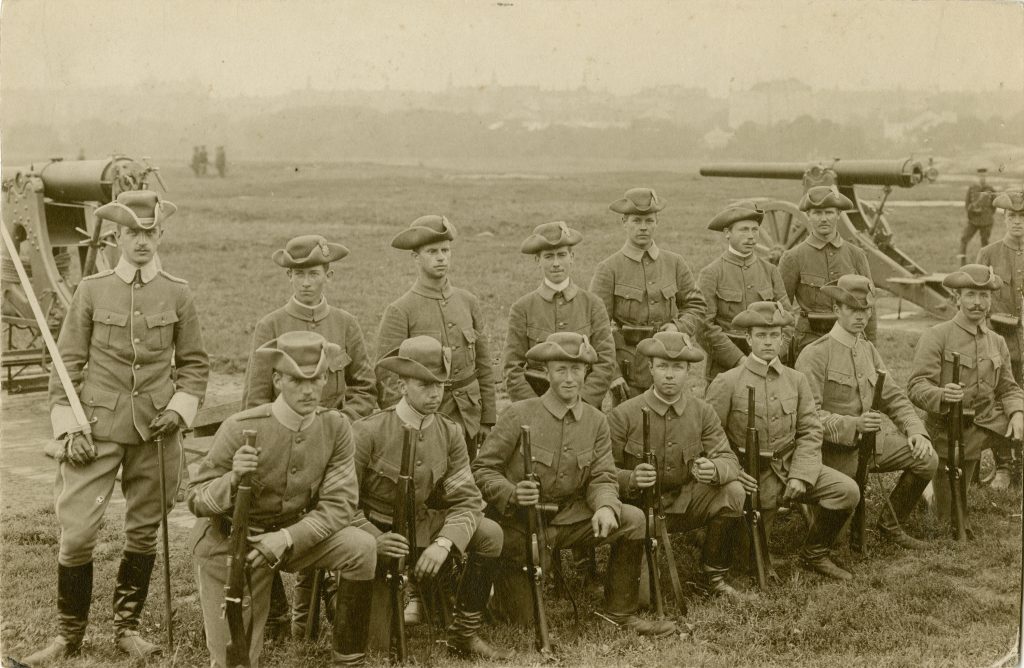 Gammalt foto på soldater med gevär i händerna framför en kanon
