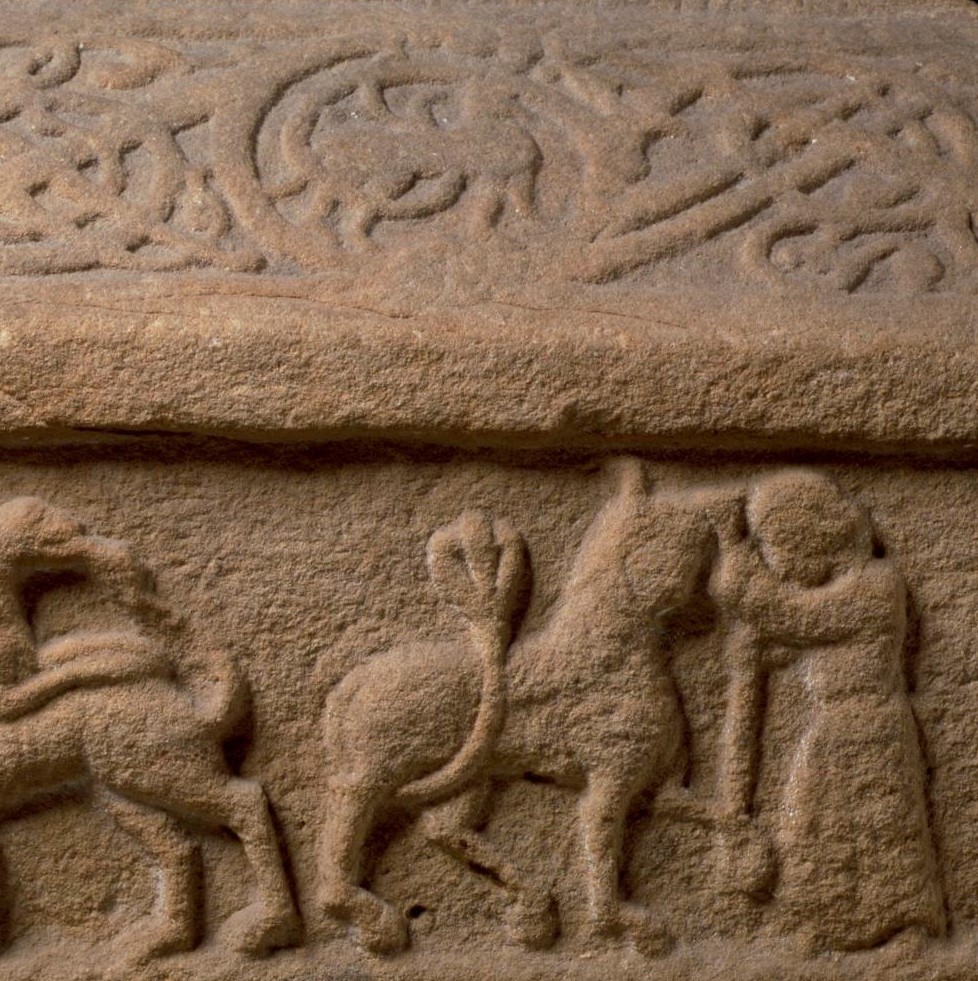 En huggen relief i röd sandsten som visar en man som kämpar mot ett lejon.