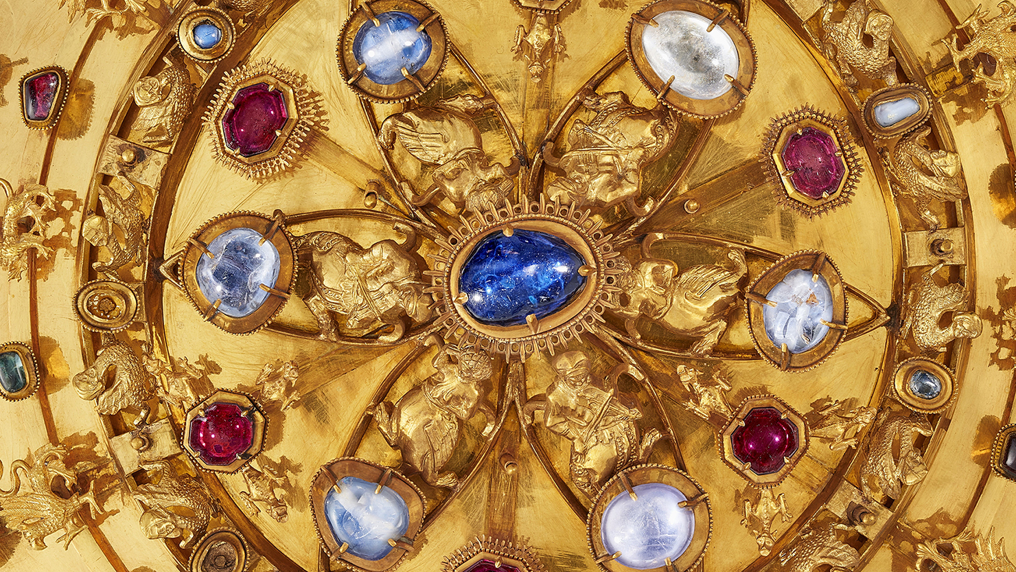 Närbild av en guldbrosch med ädelstenar i olika färger.