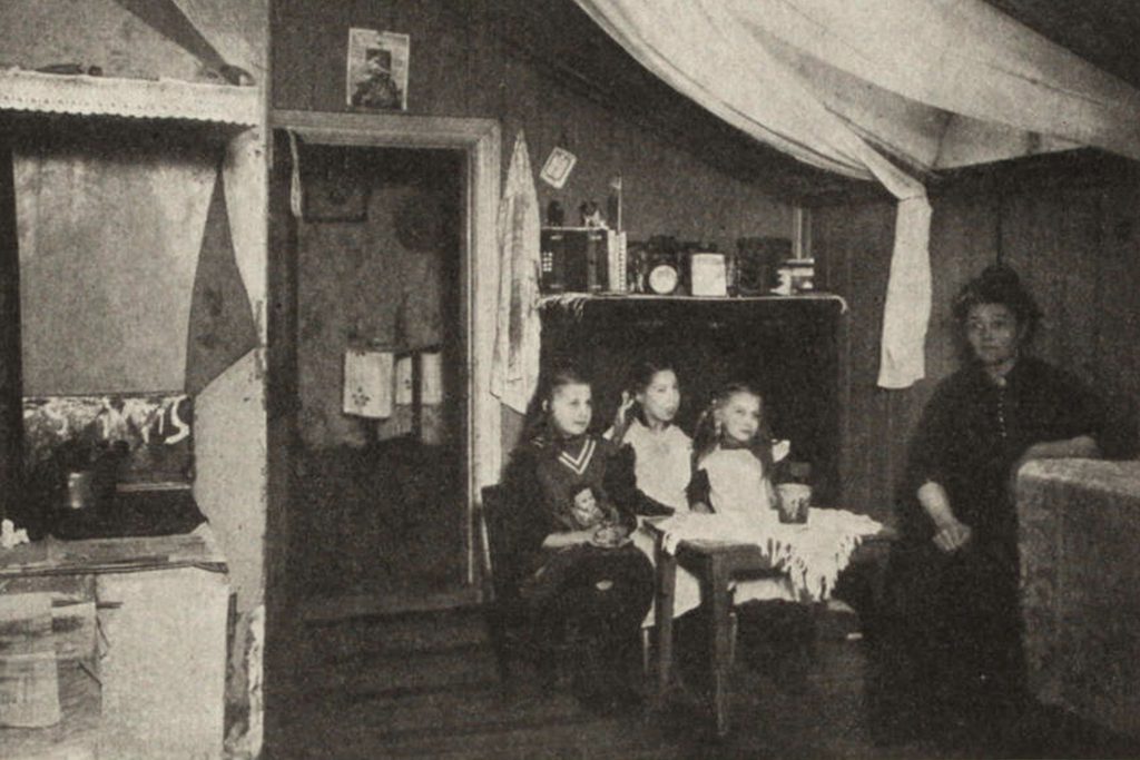Ett litet rum med en spis. Vid ett bord sitter tre barn och en kvinna.