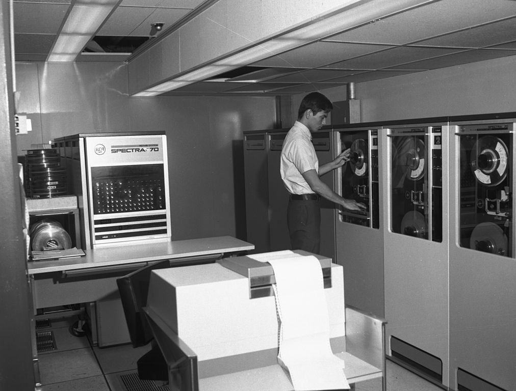 En man står och arbetar vid en gammal datamaskin som består av flera stora skåp.