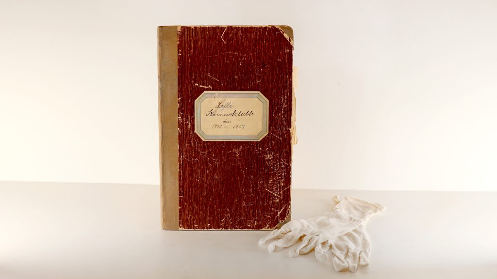 En äldre bok ståendes med ett par vita handskar liggandes bredvid.