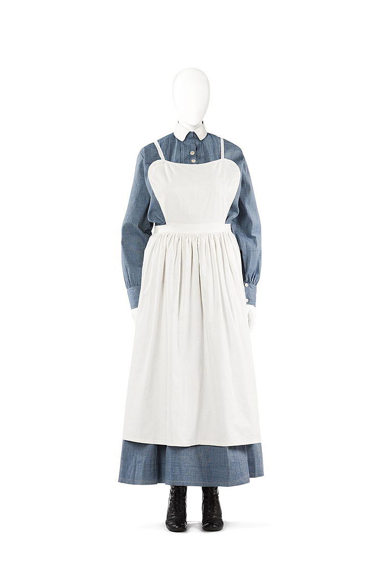 Blå klänning som går halvvägs ned på smalbenen. Ovanpå den ett vitt förkläde.