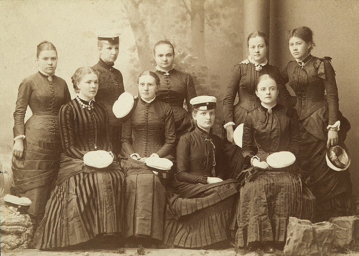 Svartvitt foto på nio unga kvinnor i svarta klänningar och med studentmössor.