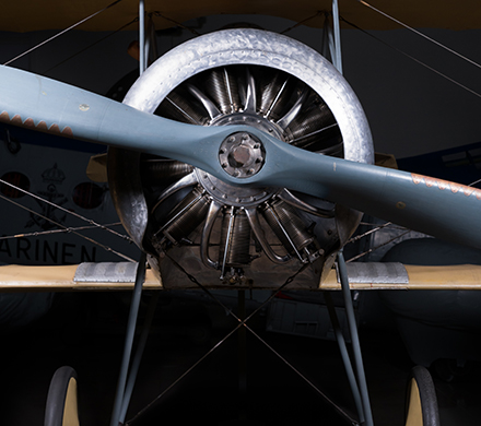 Bilden visar nosen på ett gammalt propellerflygplan. Planet är stålgrått och bakgrunden mörk.