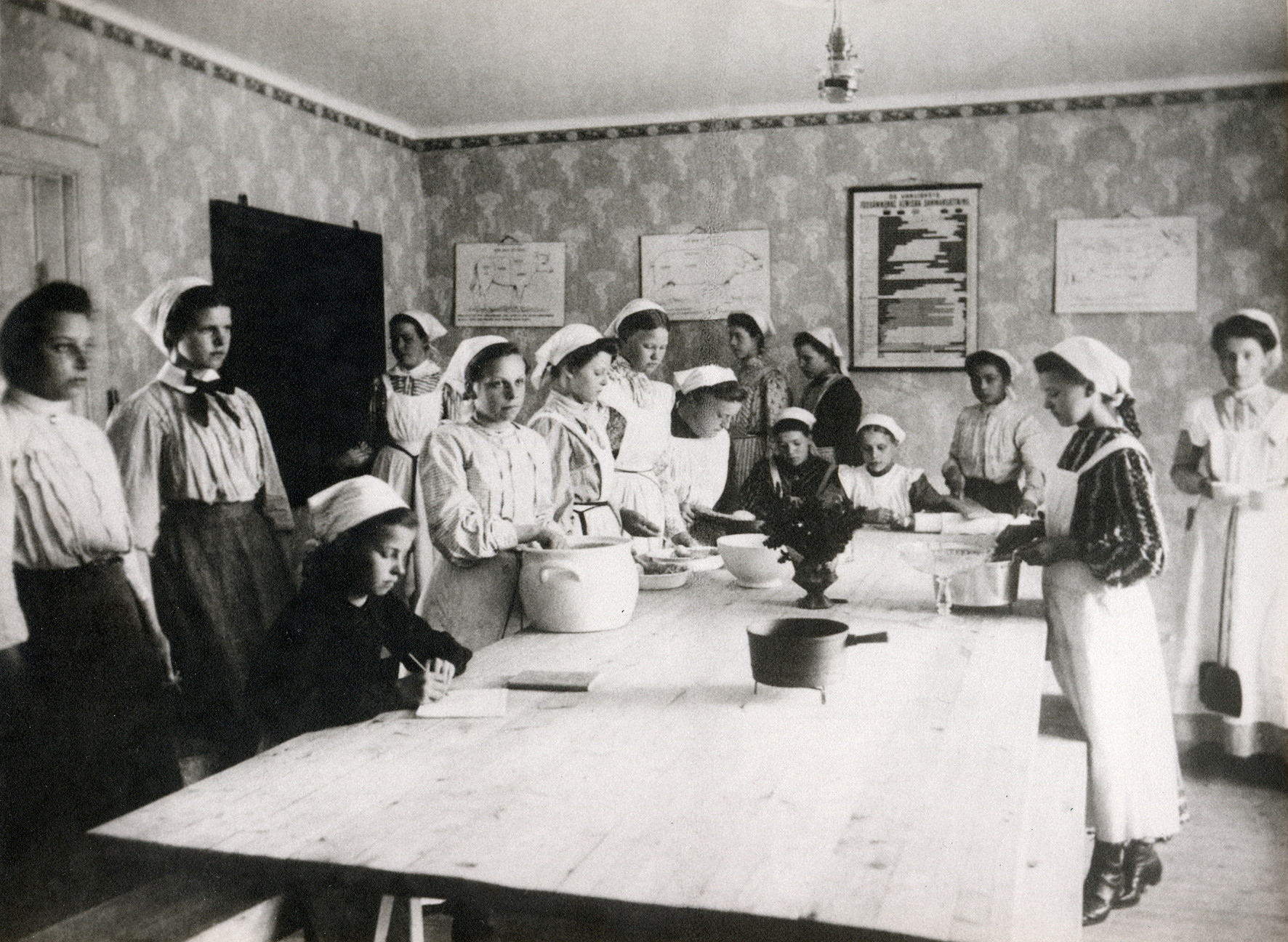En grupp flickor i vita förkläden som lagar mat vid ett bord.