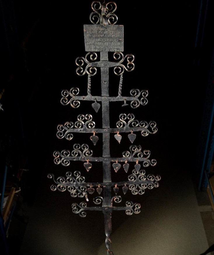 Ett svart smideskors med en mängd hängande dekorationer.