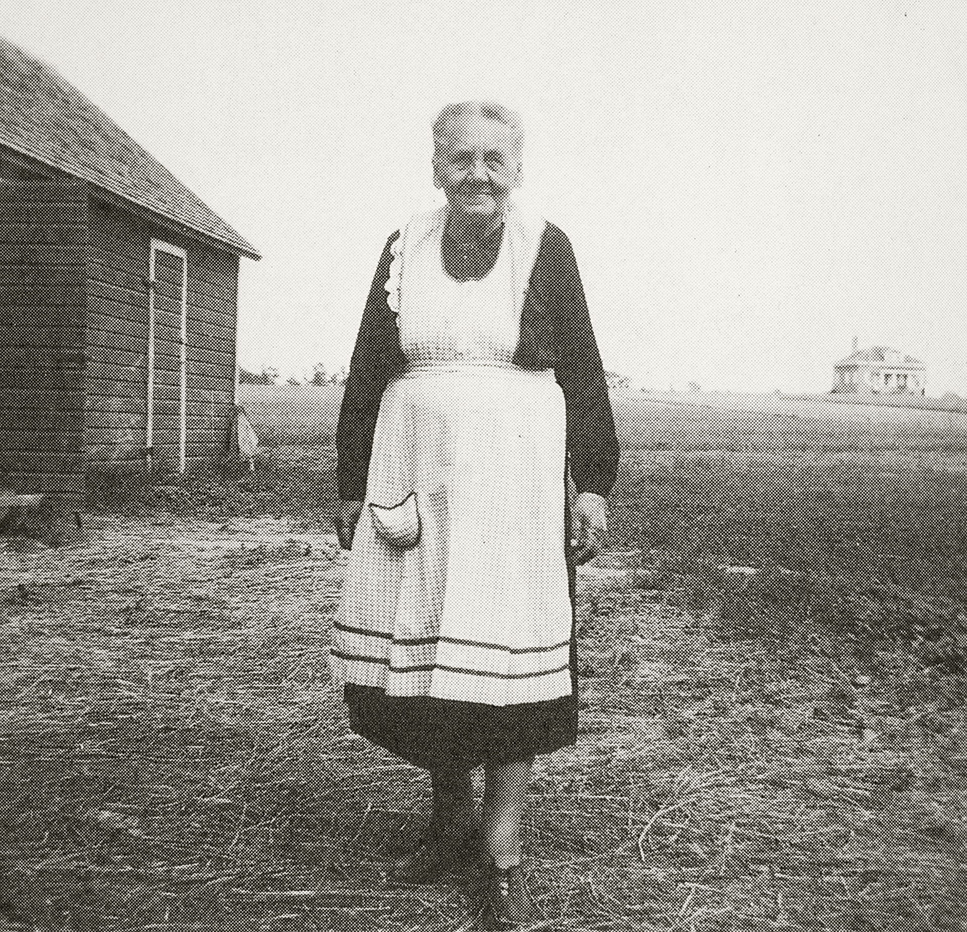 Svartvitt fotografi av en äldre kvinna med mörk klänning och vitt förkläde.