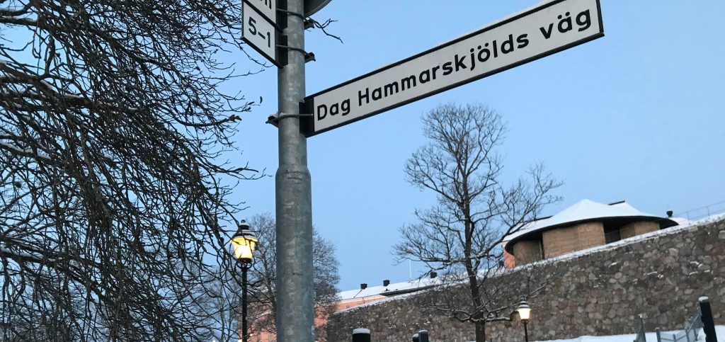 Gatuskylt med texten Dag Hammarskjölds väg, mot en blå himmel.