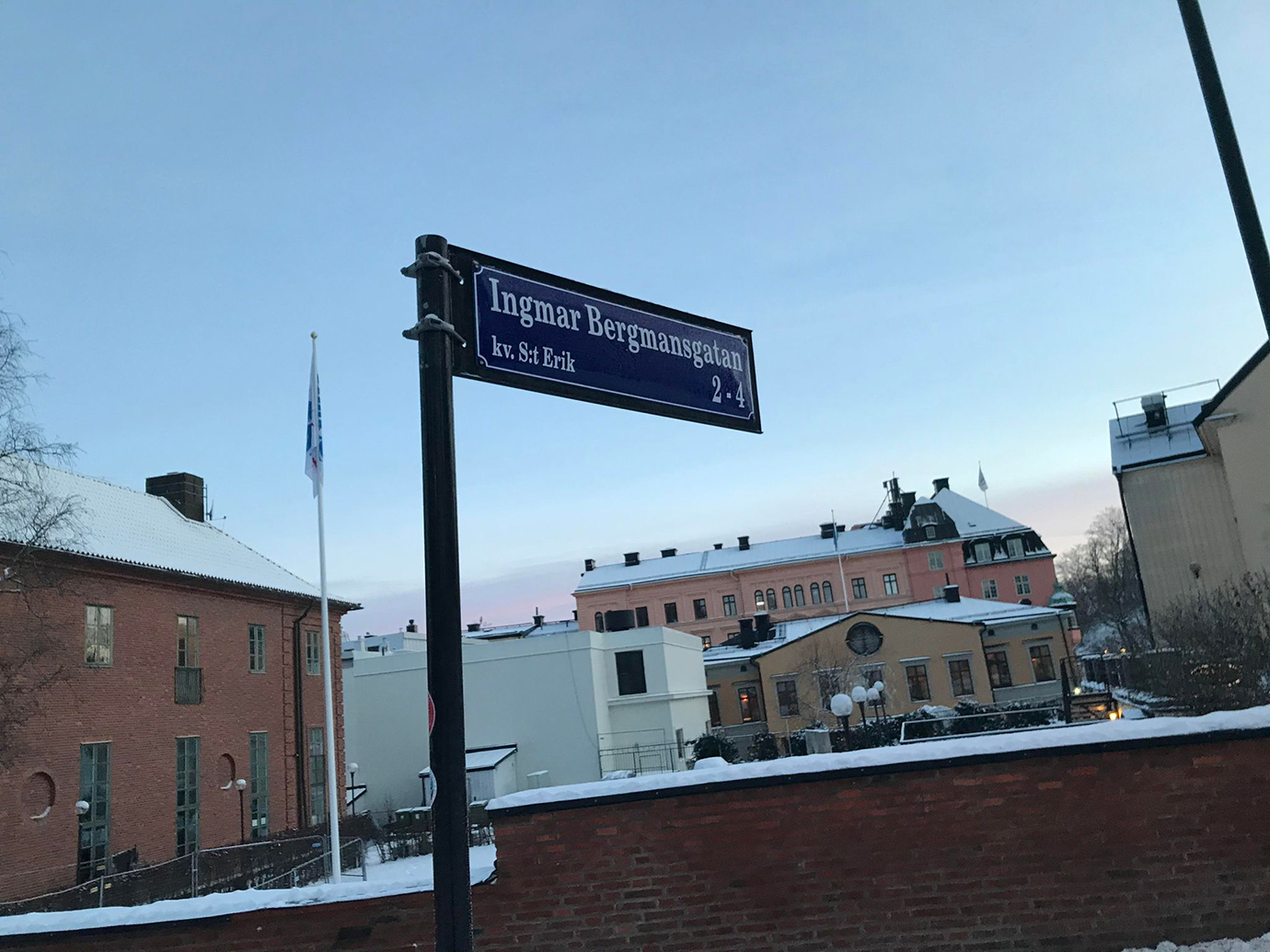 En gatuskylt med texten Ingmar Bergmansgatan. I bakgrunden syns hus med snö på taken.