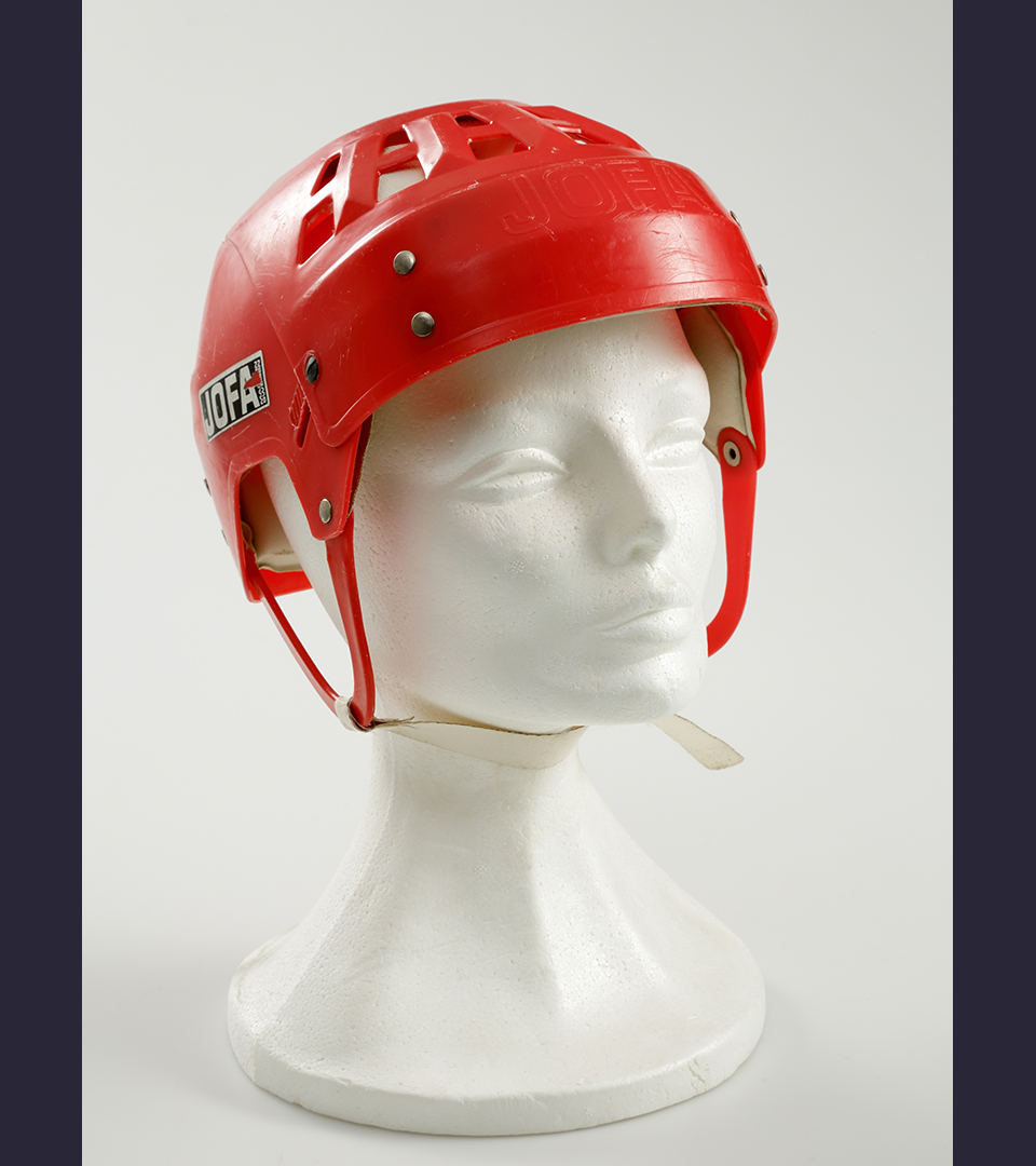 En röd ishockeyhjälm som sitter på ett frigolithuvud.