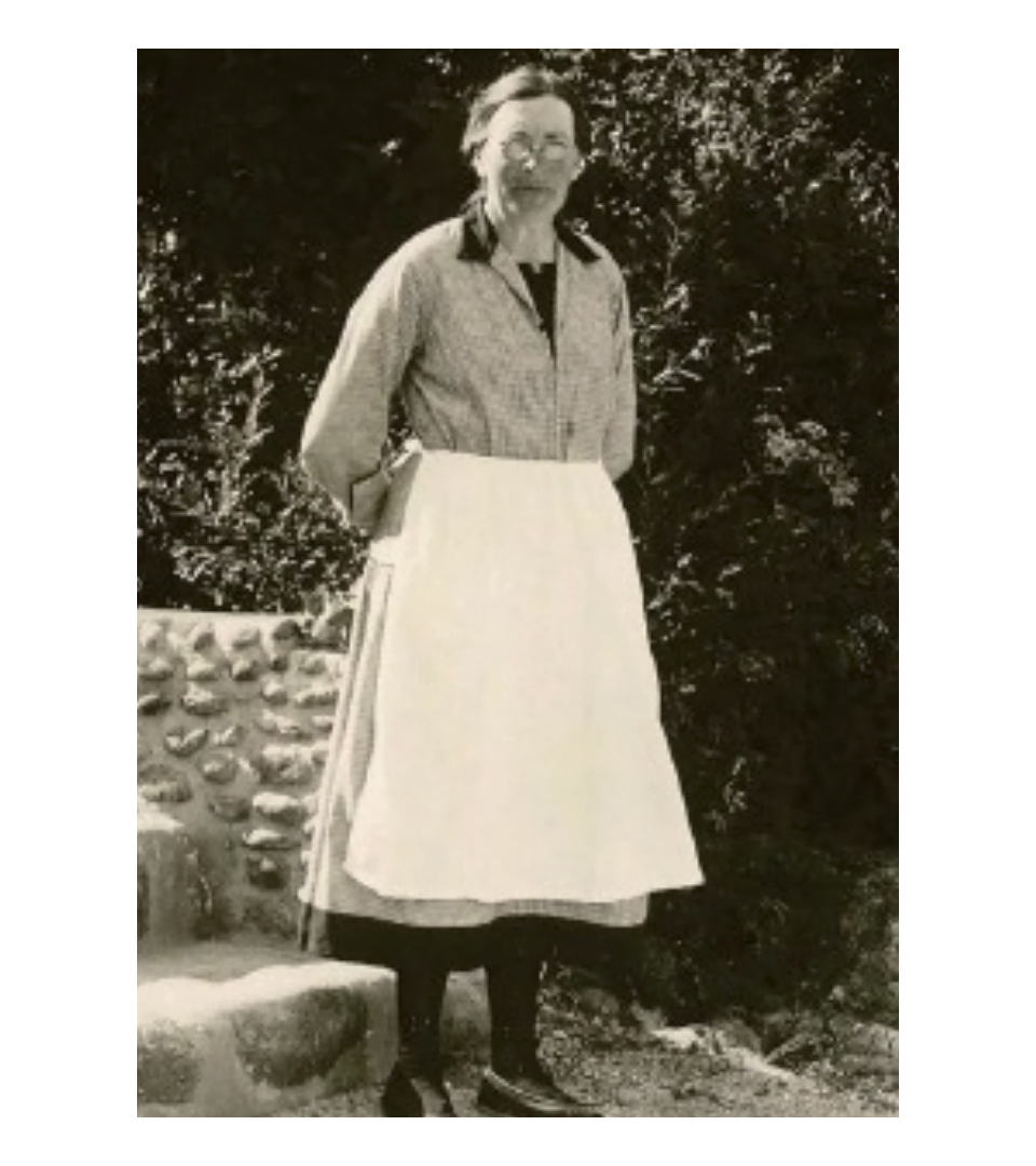 Svartvitt foto av en kvinna som står framför en stentrappa med händerna på ryggen.
