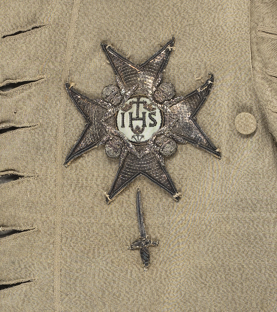 En guldbroderad stjärna med bokstäverna IHS i mitten. Under syns ett guldbroderat svärd.