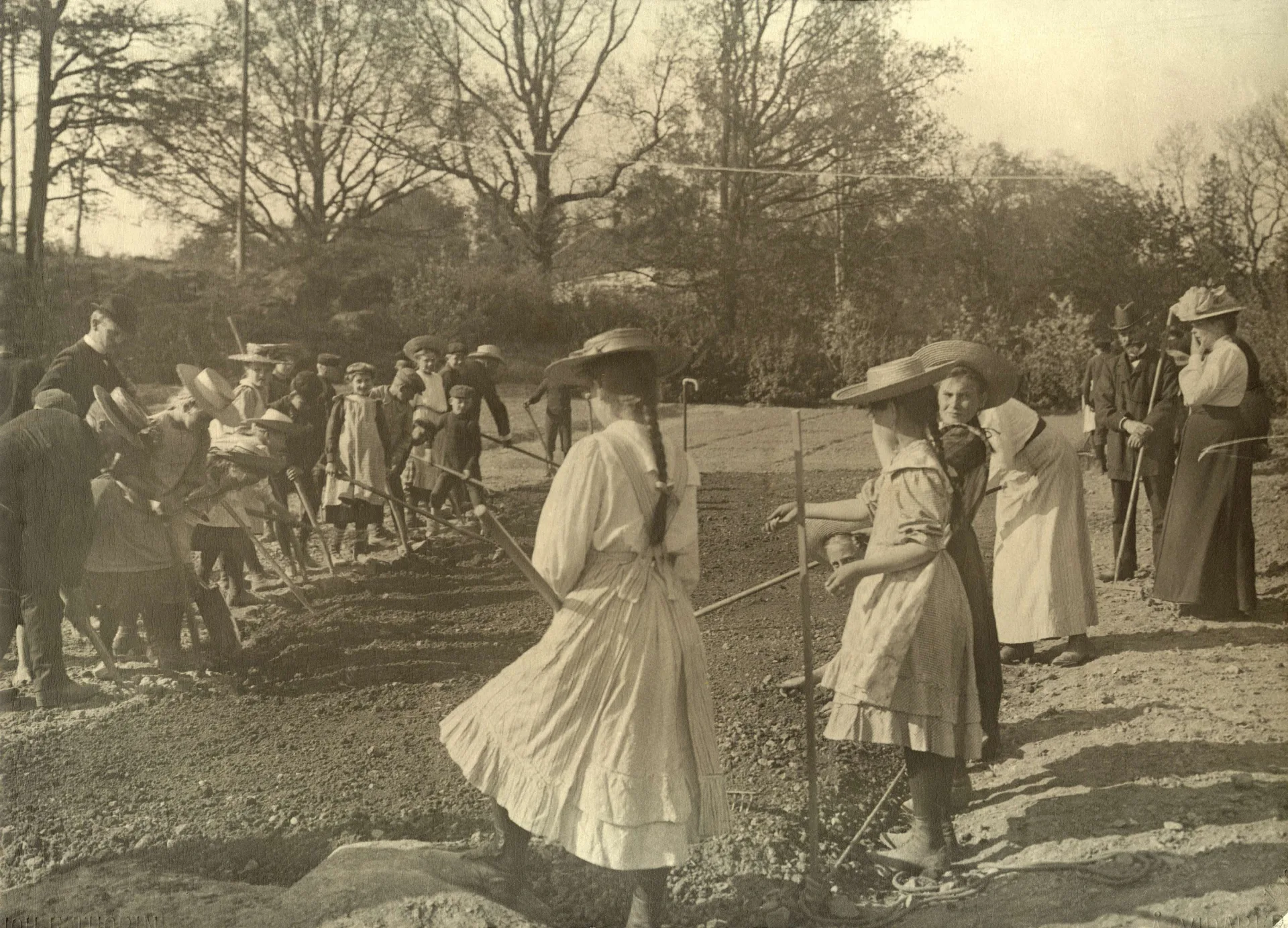 Svartvitt foto av flickor i klänningar och hattar som gräver i jorden.